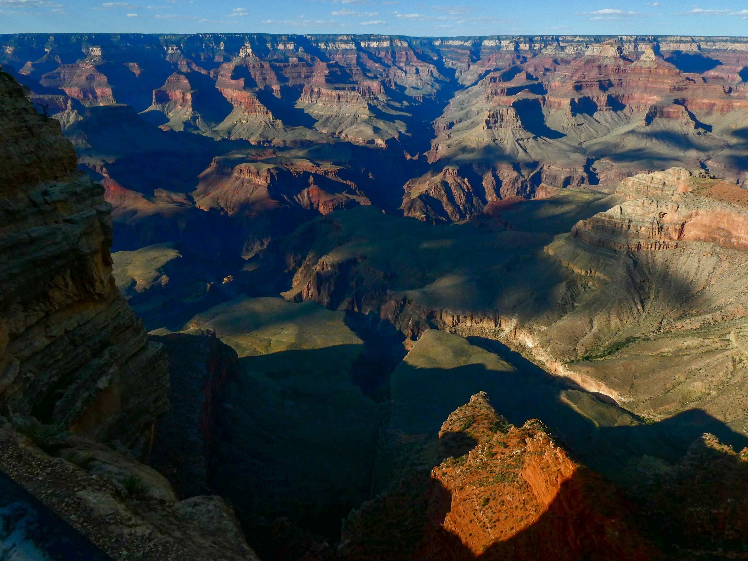 Rolling canyons and plateaus folding ever on with blueish reds smeared across greenish tan filling the picture with a streak of blue sky at the top.